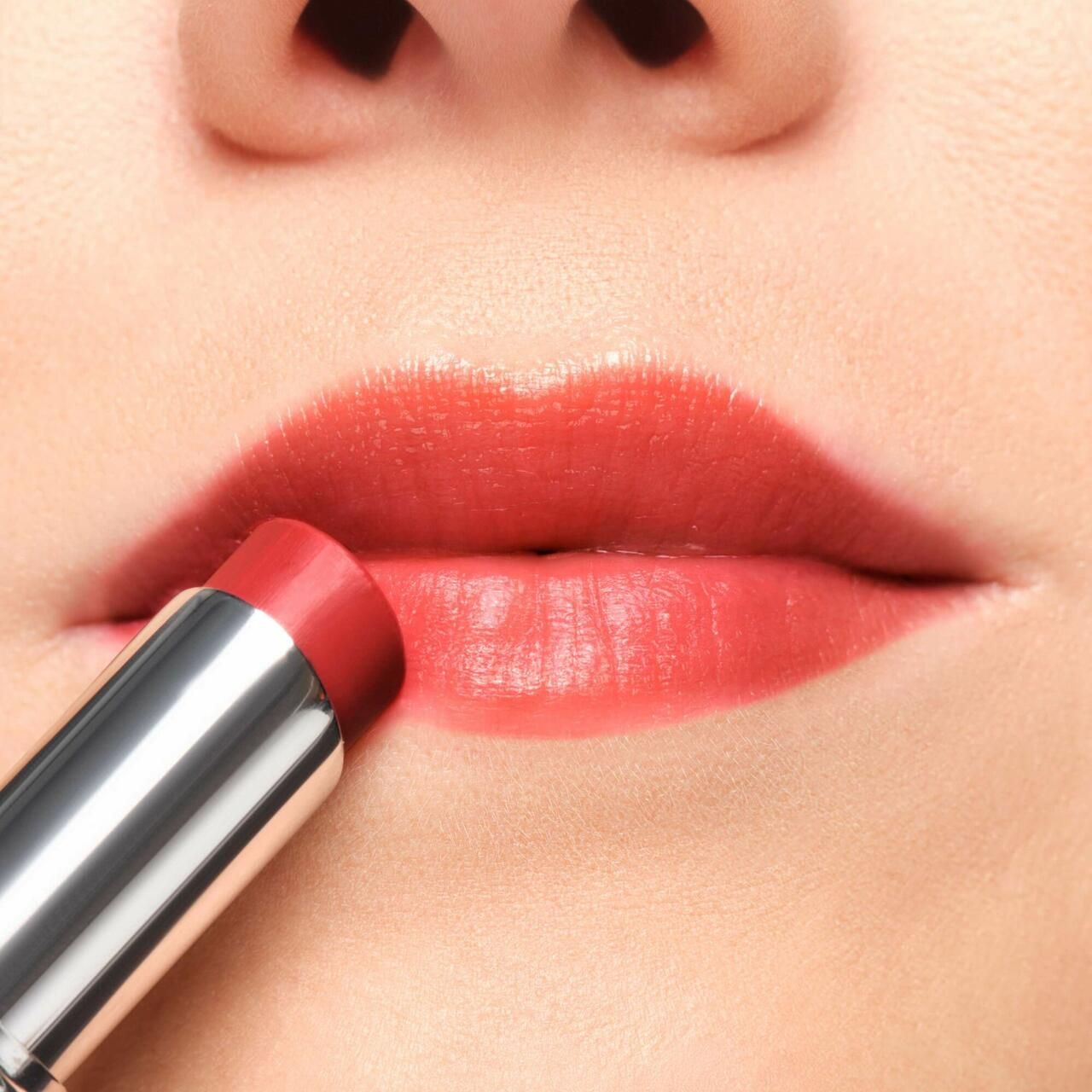 Primo piano di labbra truccate con un balsamo labbra color corallo. Astuccio argentato.