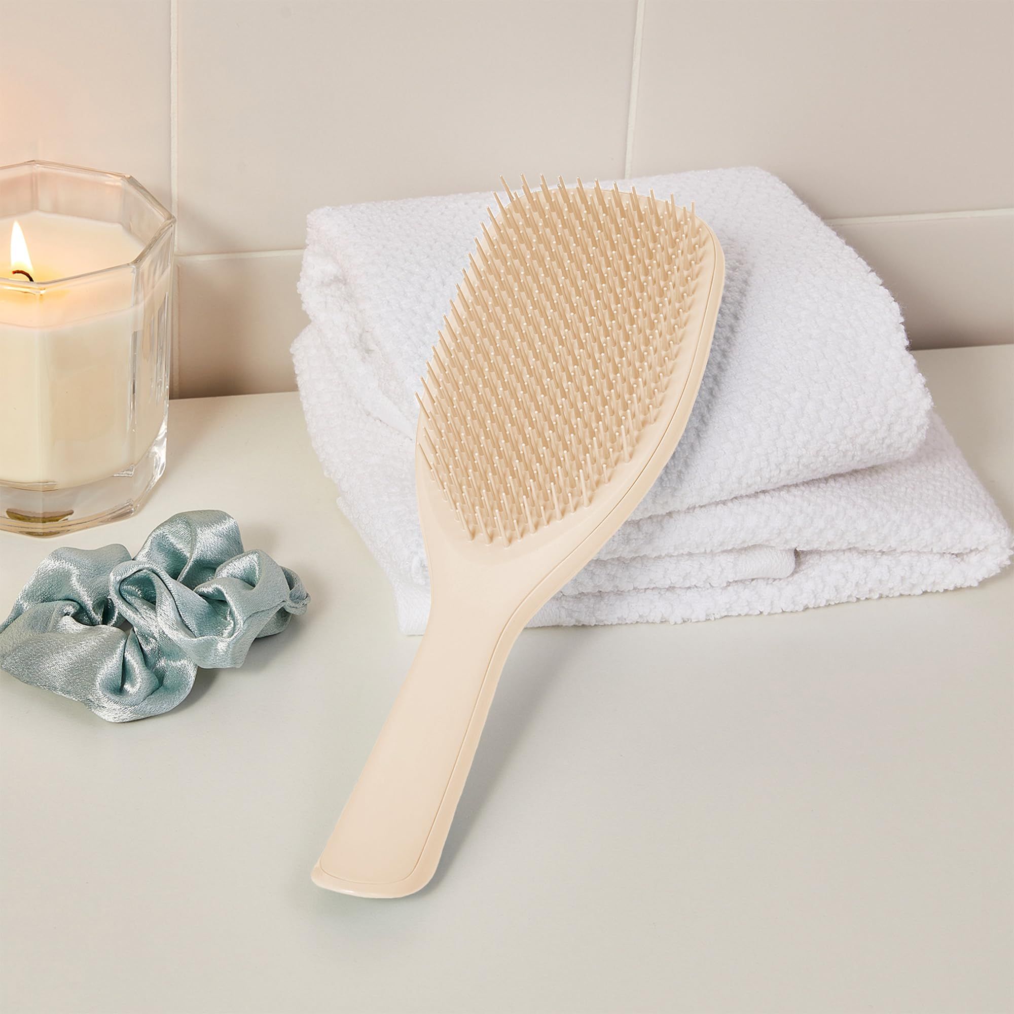 Spazzola per capelli color crema con manico su una superficie bianca. Accanto a asciugamani e un portacandele.