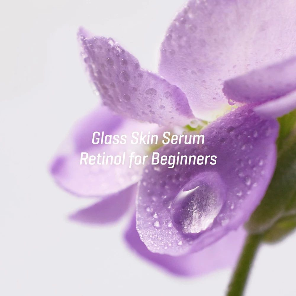 Primo piano di un fiore viola con gocce d'acqua. Testo: Glass Skin Serum Retinol for Beginners.