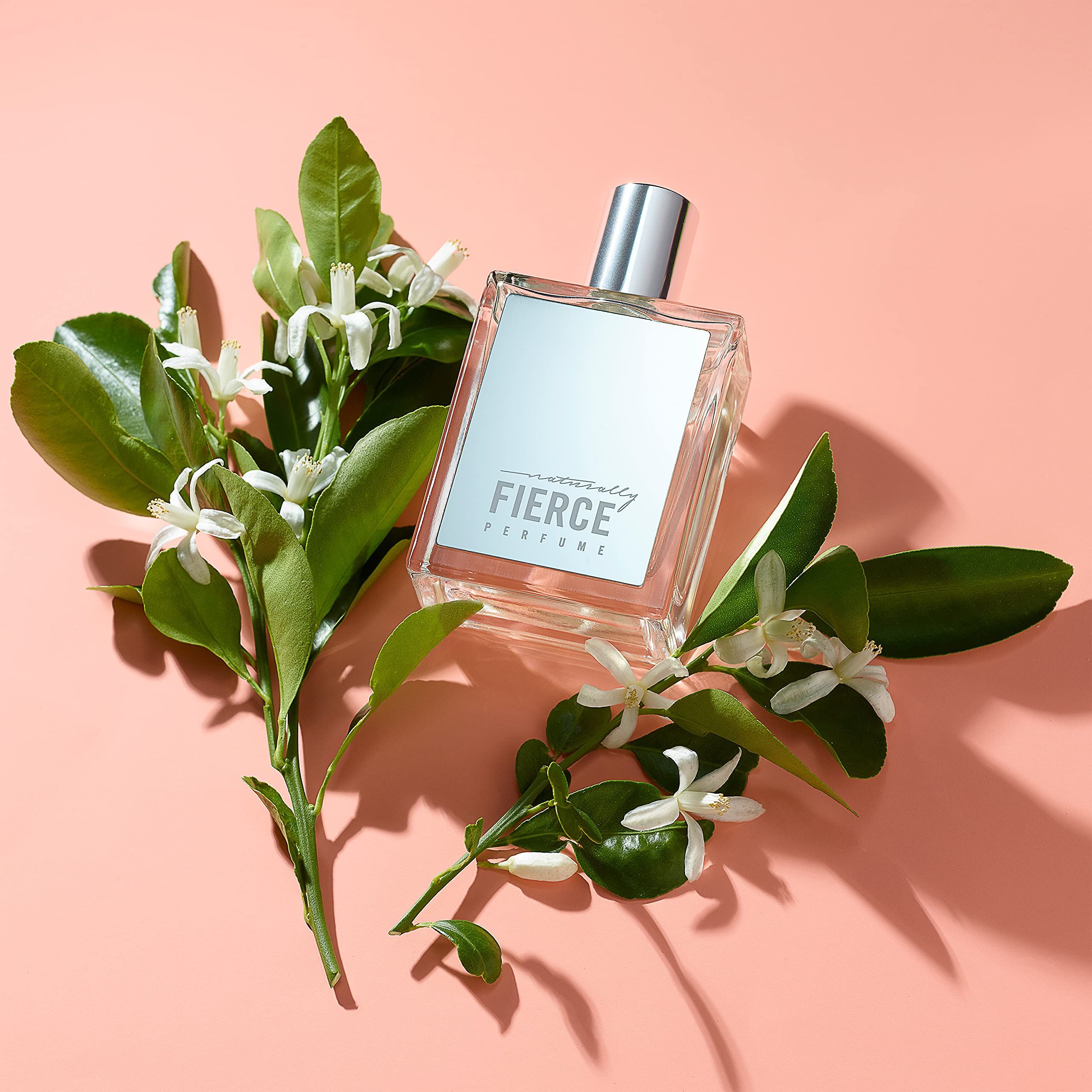 Flacone di profumo con fiori e foglie su sfondo rosa. L'etichetta riporta "FIERCE".