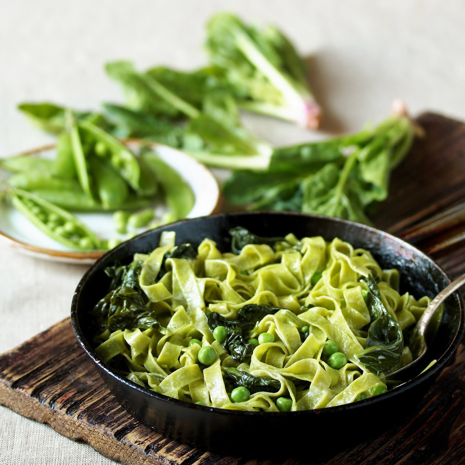 Padella con tagliatelle verdi, piselli e spinaci. Su un tagliere, con verdure.