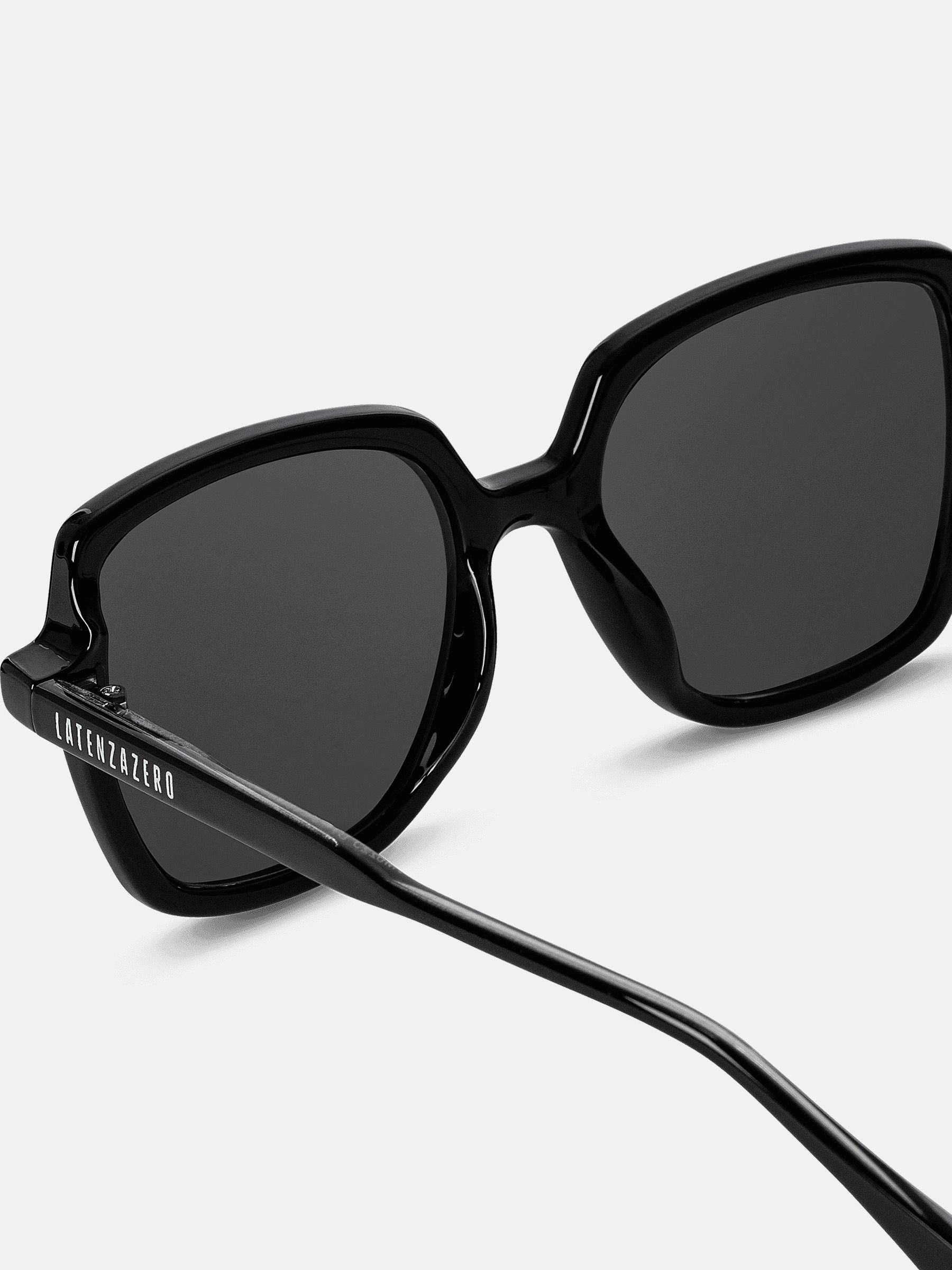 Primo piano di occhiali da sole neri. Lenti quadrate, montatura nera. Latenzazero sull'asta.
