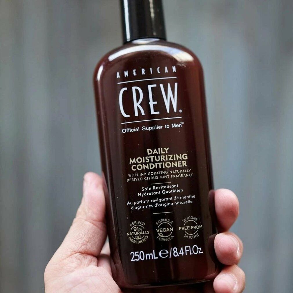 Flacone marrone tenuto in mano. Scritta: American Crew, Daily Moisturizing Conditioner. Vegano, senza silicone. 250ml/8.4 fl.oz.