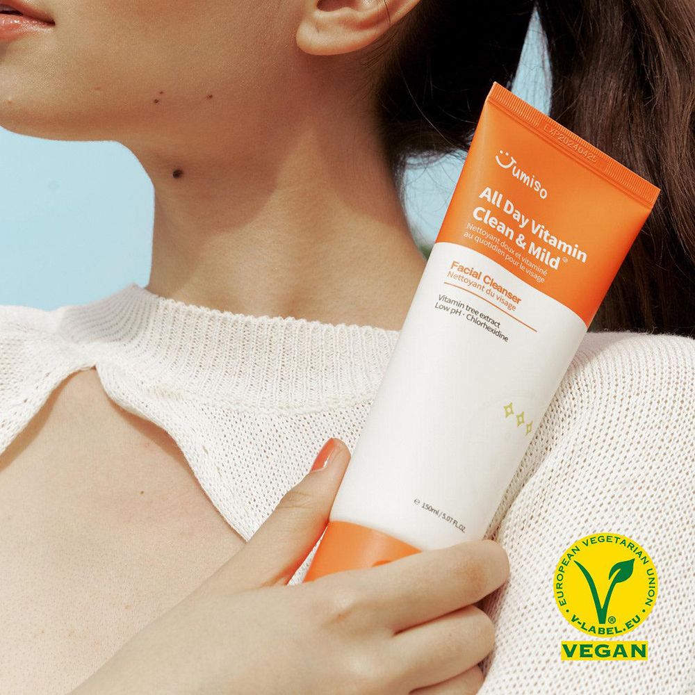 Persona che tiene un tubetto. Scritta: All Day Vitamin Clean & Mild. Sigillo vegano. Detergente viso.