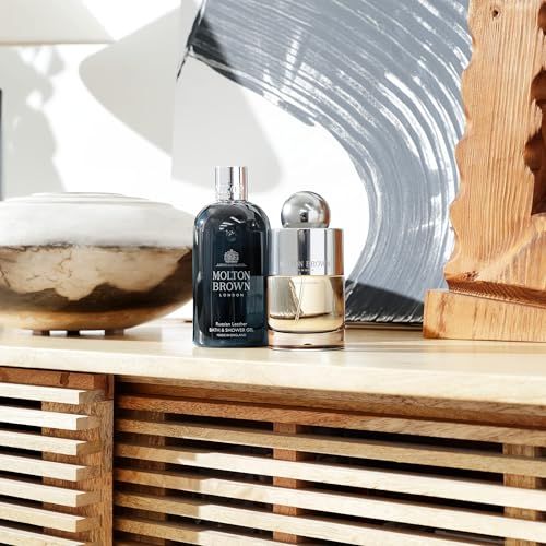 Due flaconi su una superficie in legno. A sinistra: Molton Brown. A destra: flacone con tappo argentato. Sfondo: opera d'arte.