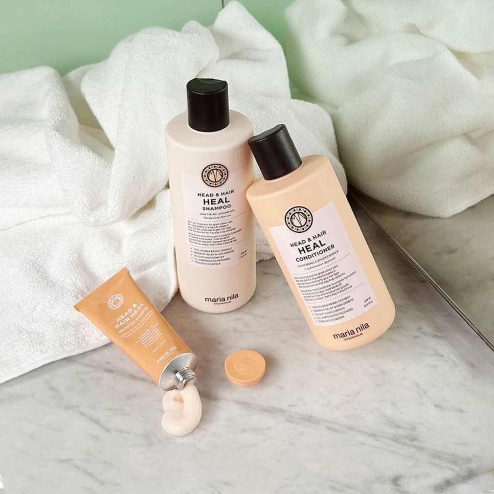 Prodotti Maria Nila: shampoo, balsamo e crema. Flaconi e tubo beige. Su superficie marmorea con asciugamani. Nomi dei prodotti visibili.