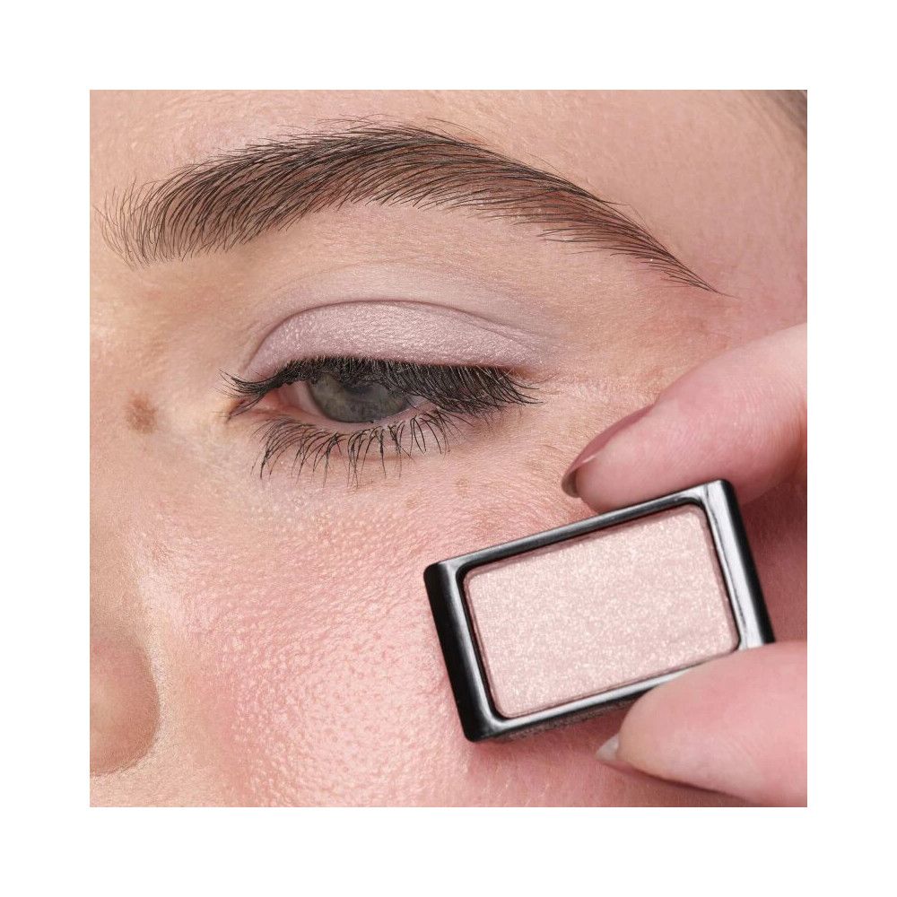 Occhio con ombretto applicato. Una mano tiene un contenitore di ombretto vicino all'occhio.