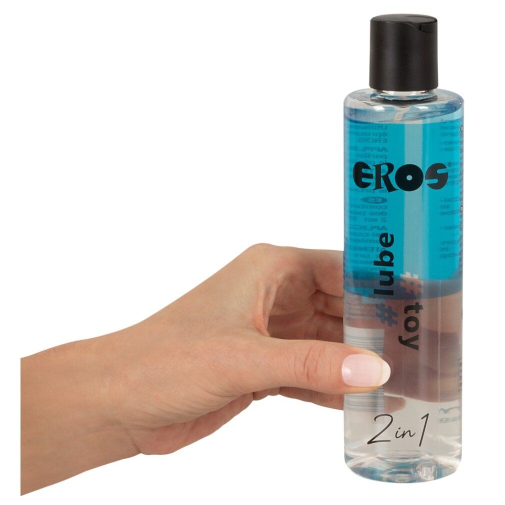 Mano che tiene una bottiglia. Scritta: EROS, #lube, #toy, 2in1. Tappo nero, liquido trasparente.
