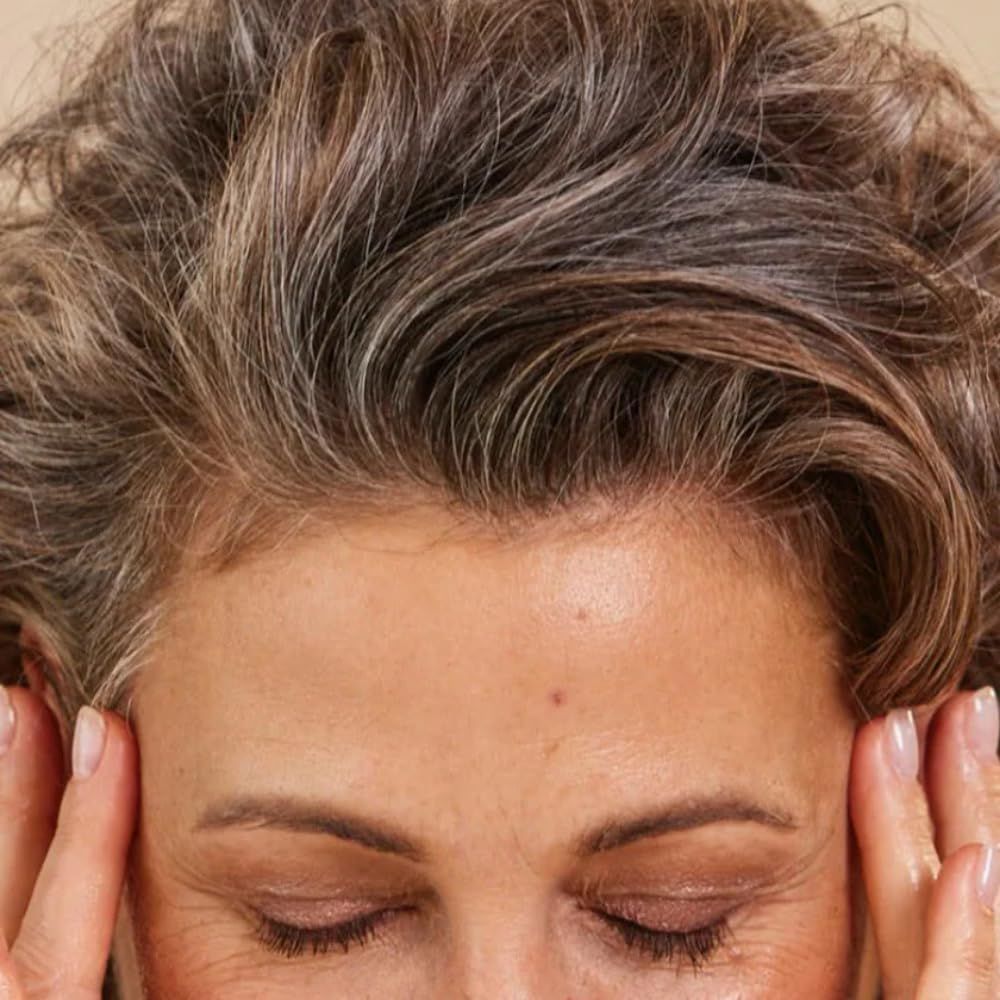 Donna con occhi chiusi, mani sulle tempie. Capelli grigi, ciocche castane.