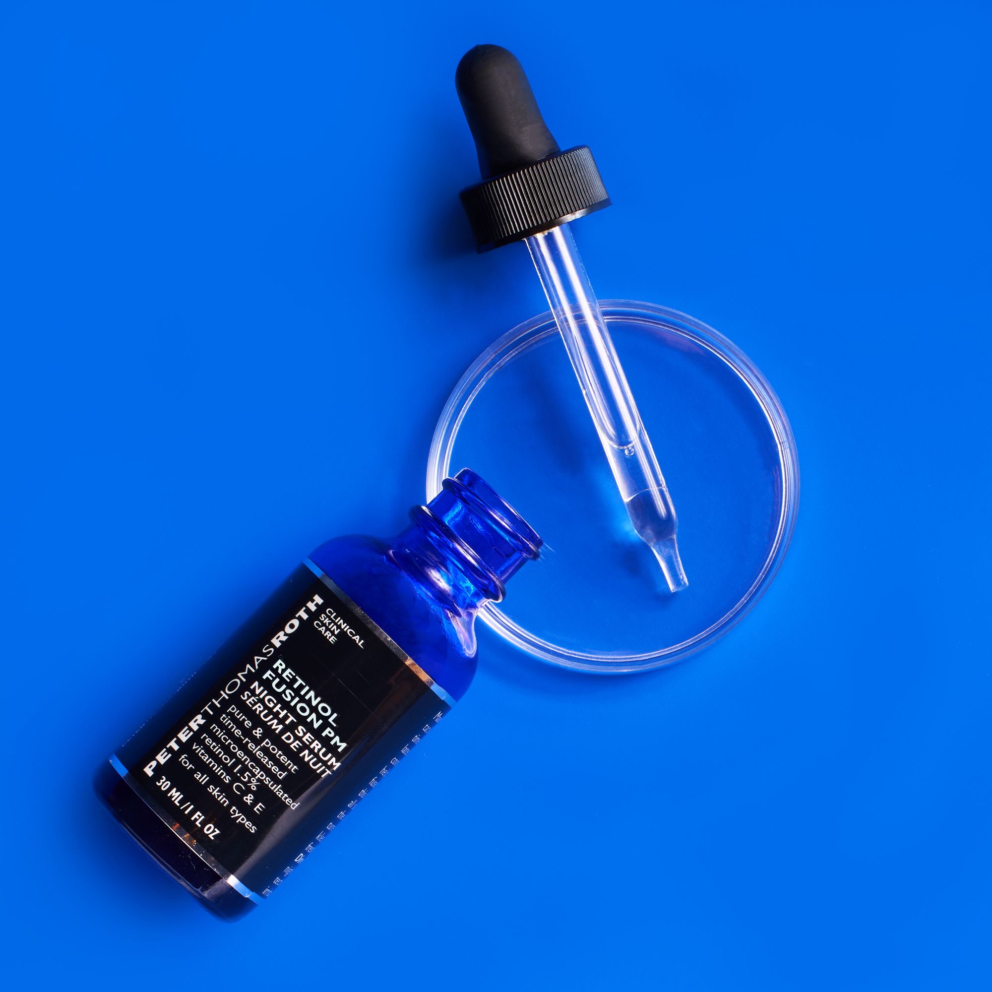 Flacone di vetro blu con tappo nero e pipetta, accanto a una capsula di Petri vuota. Sfondo blu.