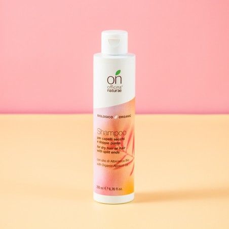 Flacone bianco con tappo verde. Scritta: "on officina naturale", "Shampoo", testo e logo. Sfondo rosa-arancio.