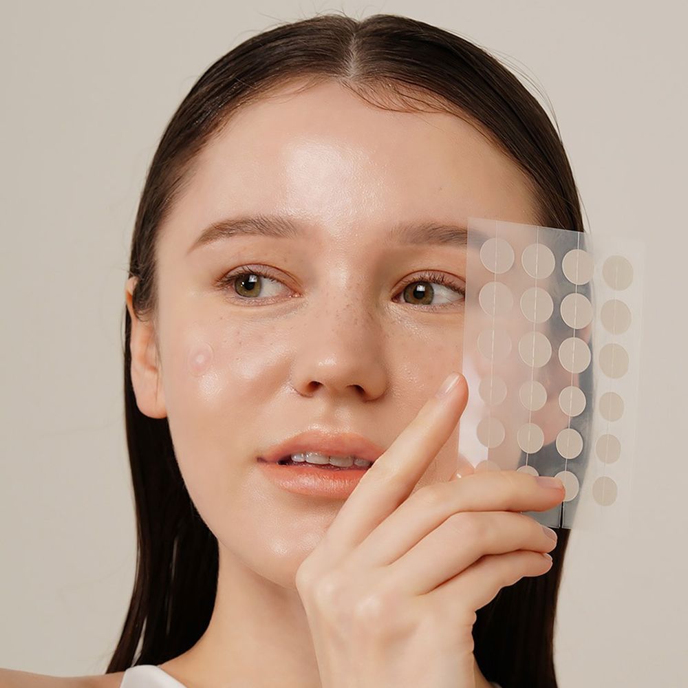 Persona tiene un foglio di cerotti rotondi e trasparenti. Alcuni cerotti sono visibili sulla pelle.