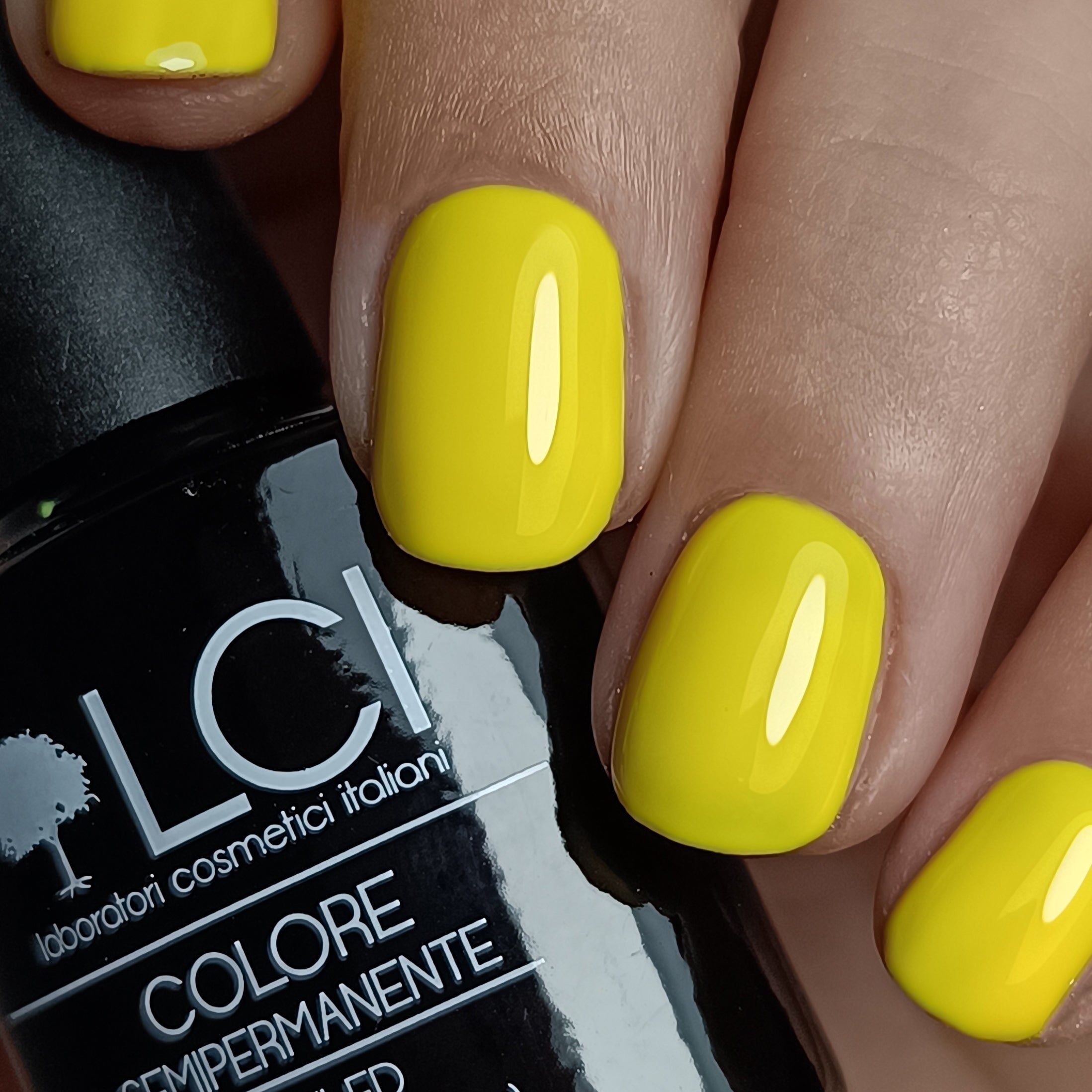Smalto gel giallo sulle unghie. Flacone nero con scritta LCI. Alcune dita con unghie smaltate.