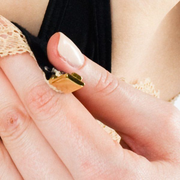 Primo piano della chiusura dorata di un reggiseno. Dita che tengono la chiusura.