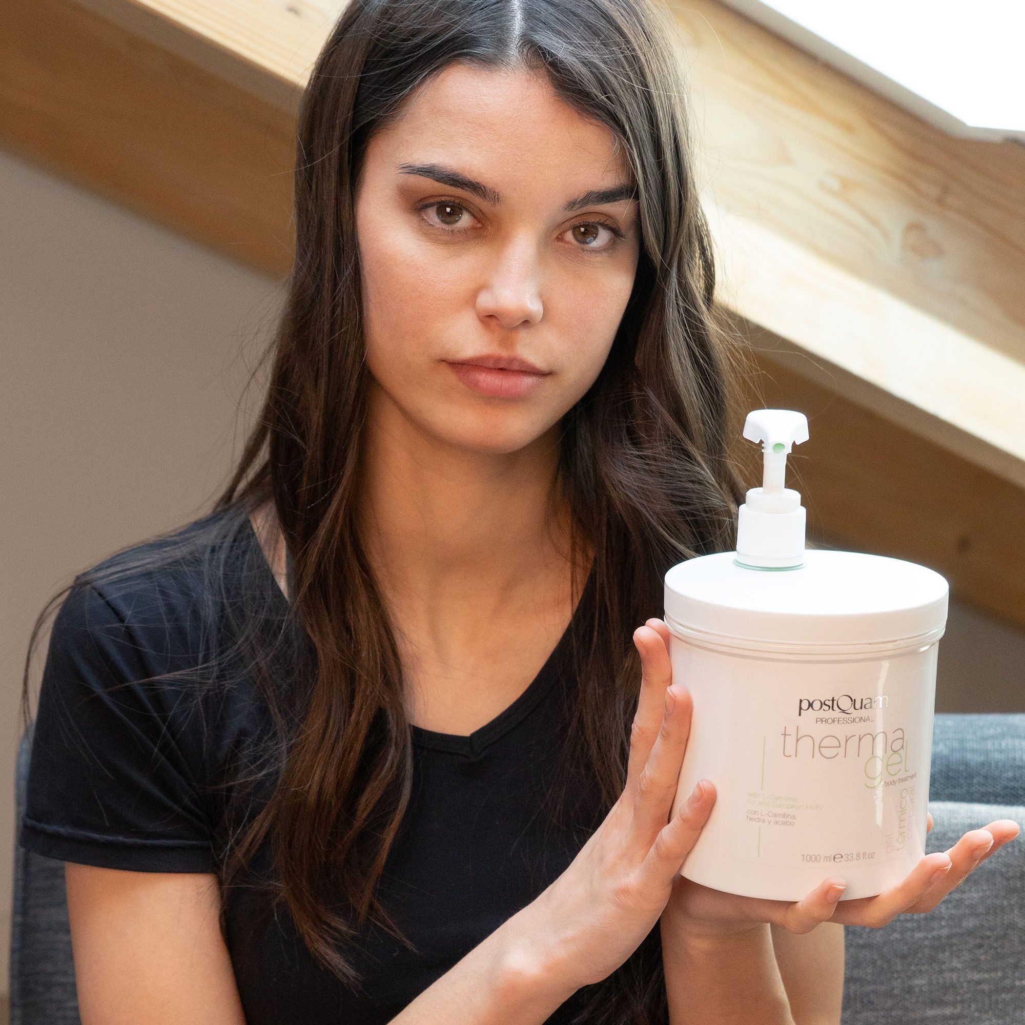 Donna tiene contenitore bianco 'PostQuam therma gel' con pompa. Indossa top nero.
