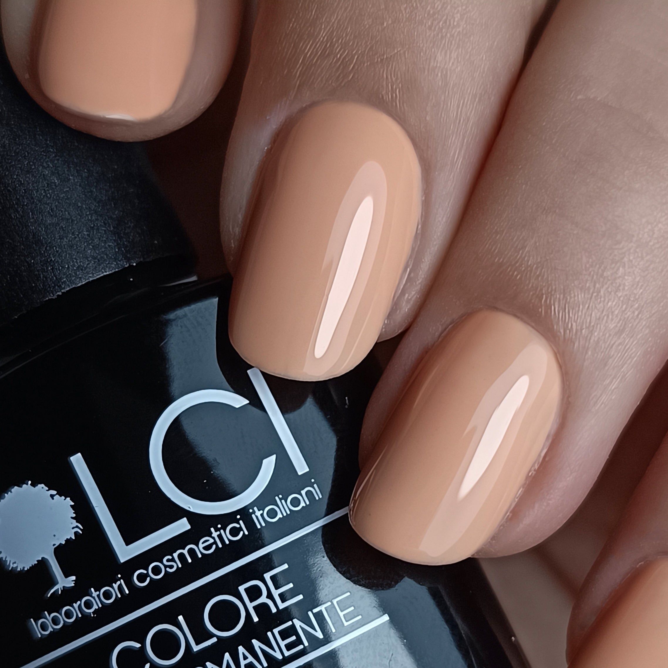 Unghie smaltate con smalto nude. Flacone con logo e testo sullo sfondo. Primo piano.