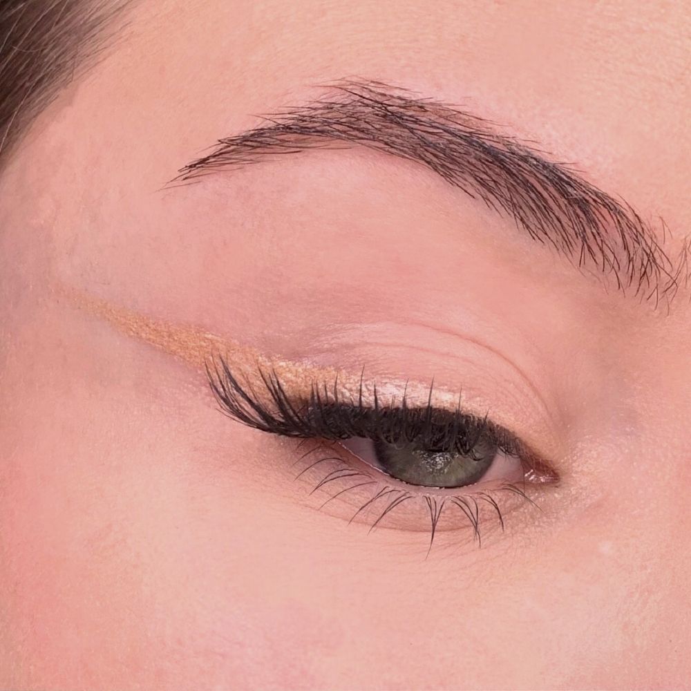 Occhio con eyeliner. Eyeliner beige sulla palpebra. Ciglia e sopracciglia visibili.