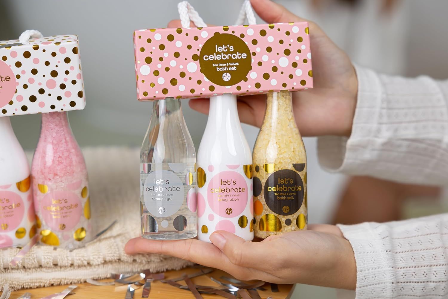 Tre bottiglie in una confezione regalo. Scritta: Let's Celebrate. Prodotti: gel doccia, lozione mani e corpo, sali da bagno. Confezione rosa.