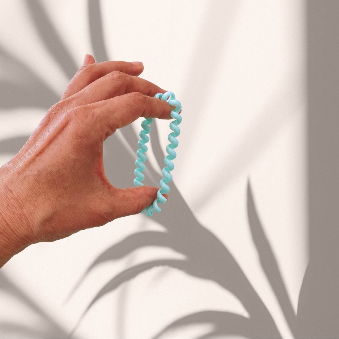Mano che tiene un elastico a spirale azzurro. Sfondo con ombre.