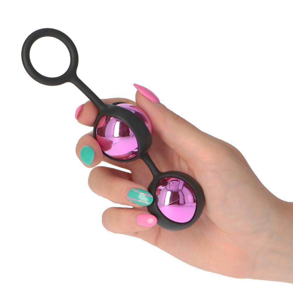 Mano che tiene due sfere rosa con connettore nero e anello. Superficie liscia. Unghie rosa e verdi.