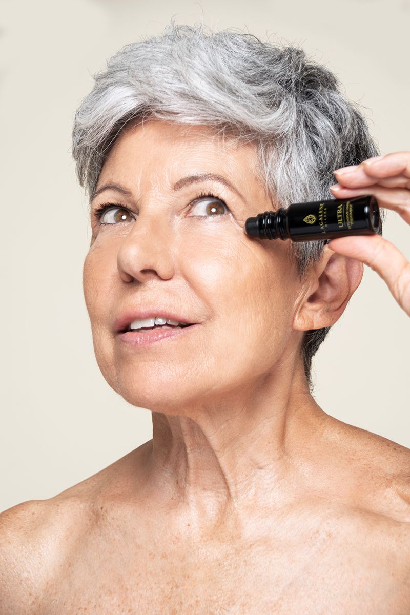 Una donna tiene un flacone Lagalene Milano Ultra Intensive Care con applicatore roll-on vicino al suo occhio. Sul flacone è scritto "ULTRA INTENSIVE TREATMENT".