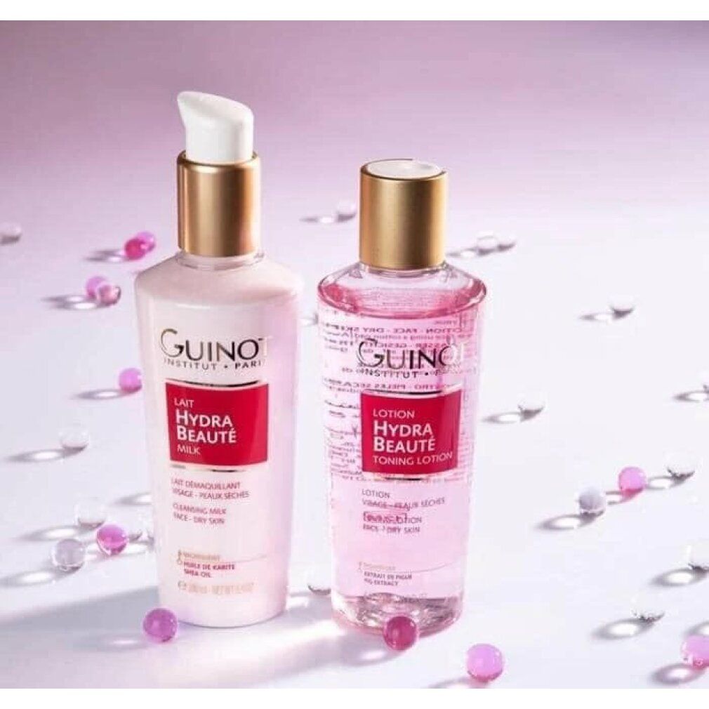 Due flaconi: Guinot Lait Hydra Beauté Milk e Lotion. Liquidi rosa, tappi dorati. Sfere sparse.