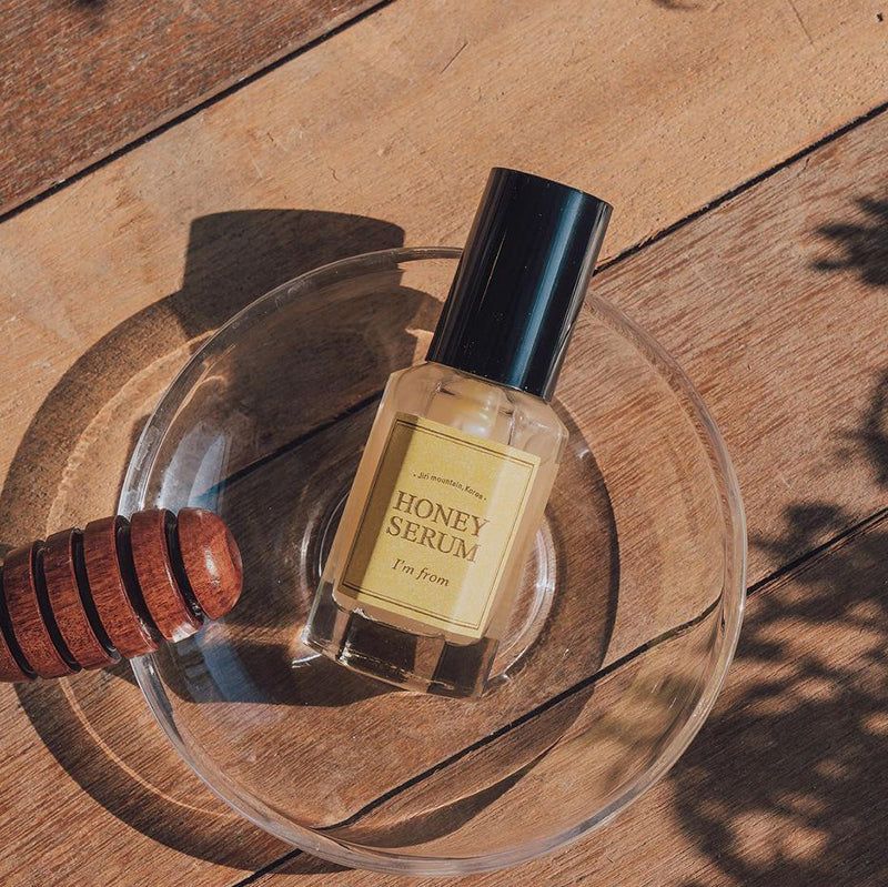 Flacone di siero su piatto di vetro. Honey Serum, I'm from. Tappo nero, etichetta gialla. Sfondo in legno, mescolatore di miele.