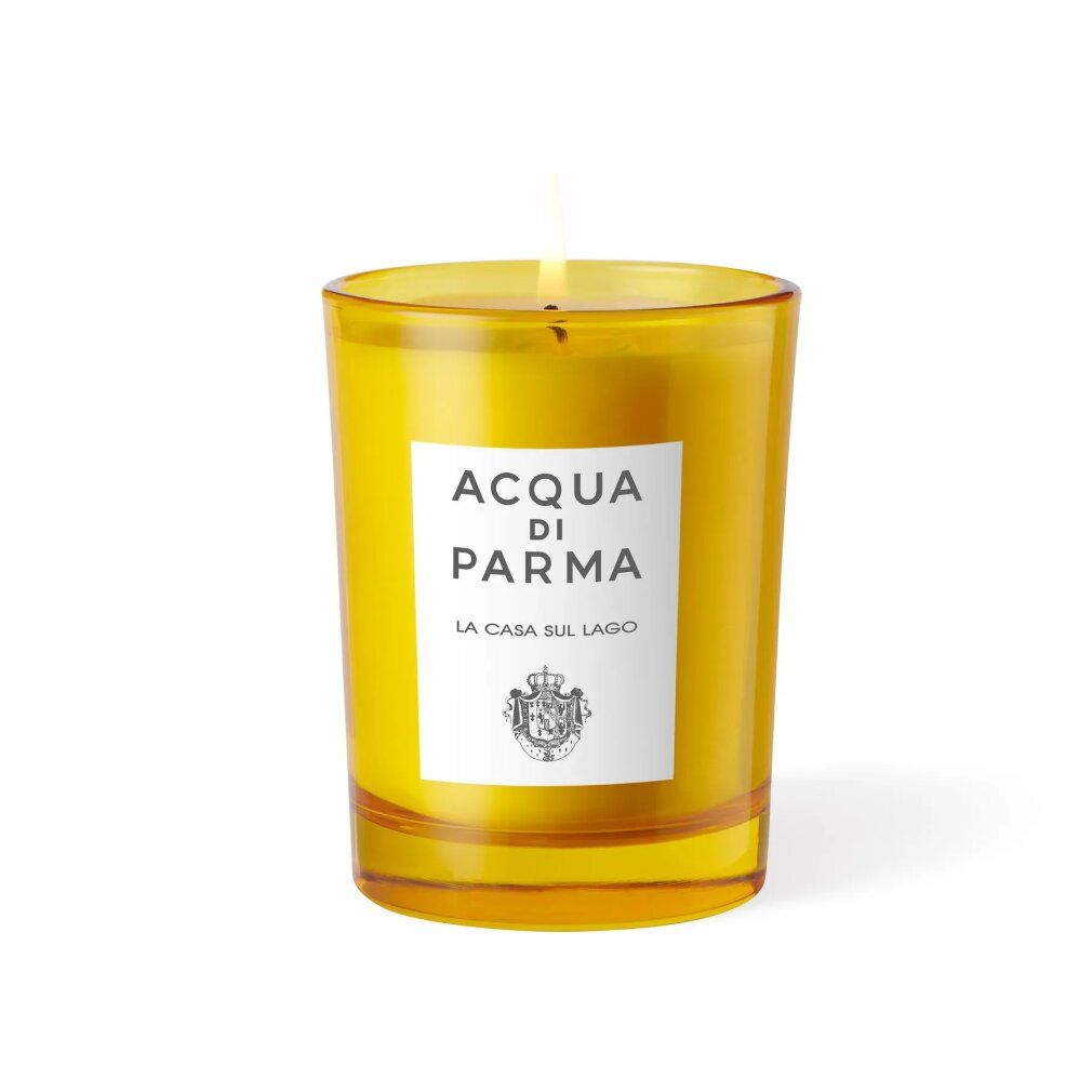 Candela gialla in contenitore di vetro. Etichetta bianca con logo e scritta. Fiamma accesa.