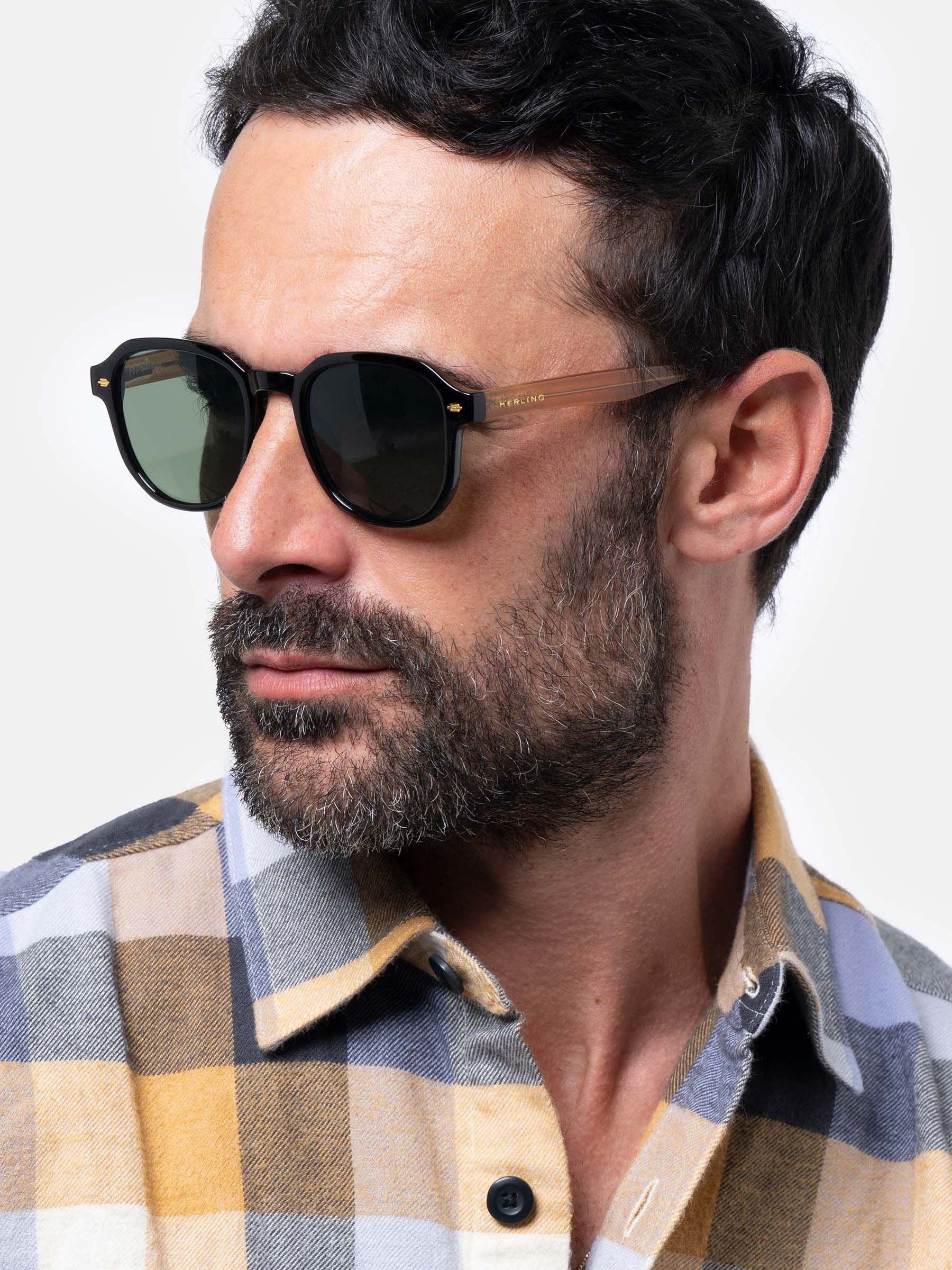 Uomo con occhiali da sole neri e marroni. Lenti verdi. Logo Herling visibile.