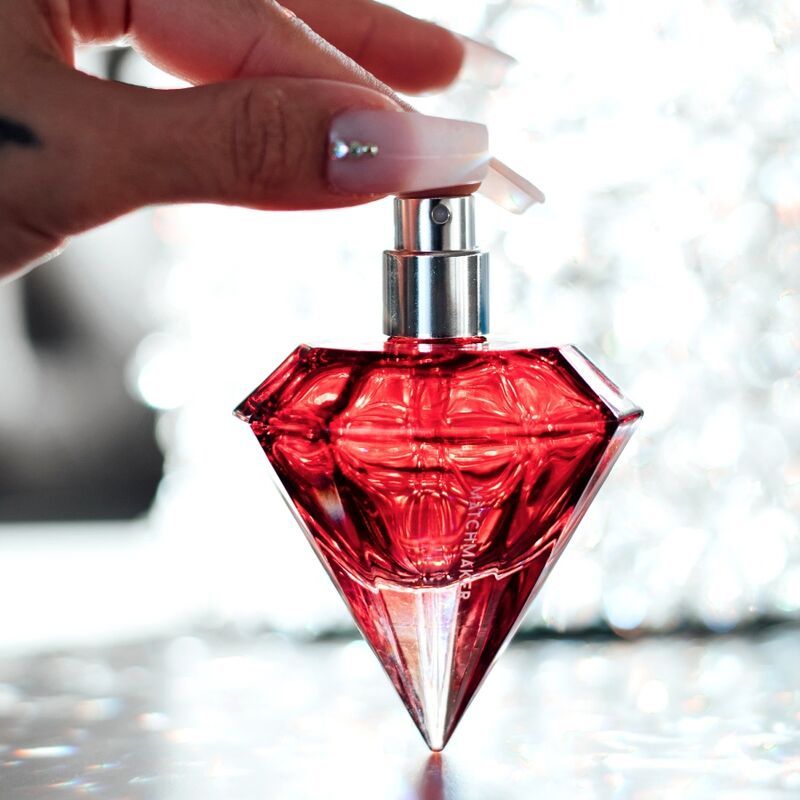 Mano che tiene un flacone di profumo rosso a forma di diamante con spruzzatore argentato.