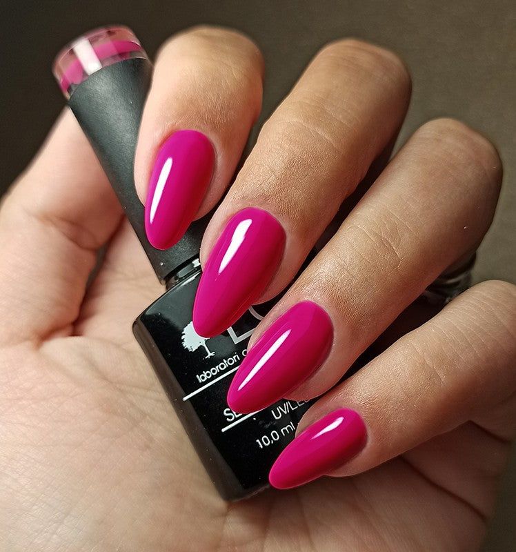 Mano con unghie smaltate e flacone di smalto. Colore: Malva-Fucsia. Flacone nero con etichetta.