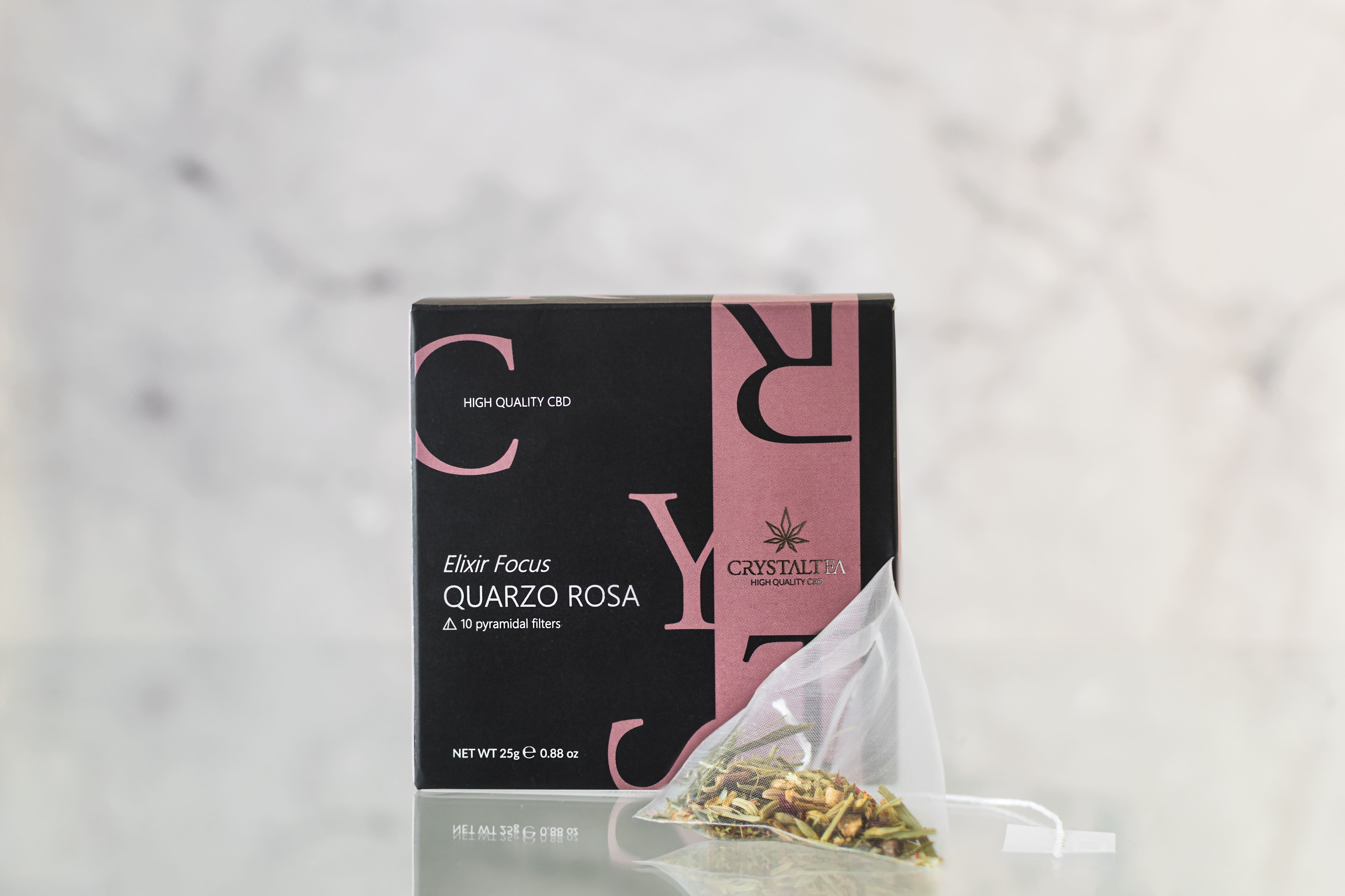 Scatola nera con testo rosa. Testo: Elixir Focus Quarzo Rosa. Accanto, una bustina di tè con erbe.