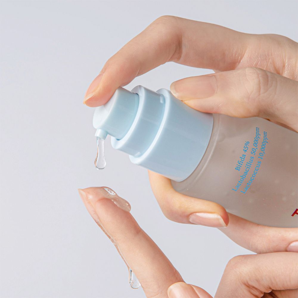 Una mano preme una goccia di liquido da un flacone. La goccia cade su un dito.