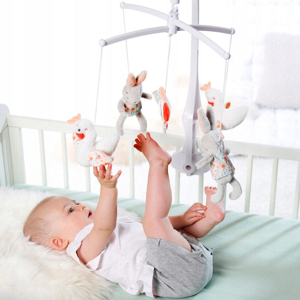 Bambino sotto il mobile, che lo afferra. Mobile con conigli, cigni e specchio. Struttura bianca. Accenti rosa e blu.