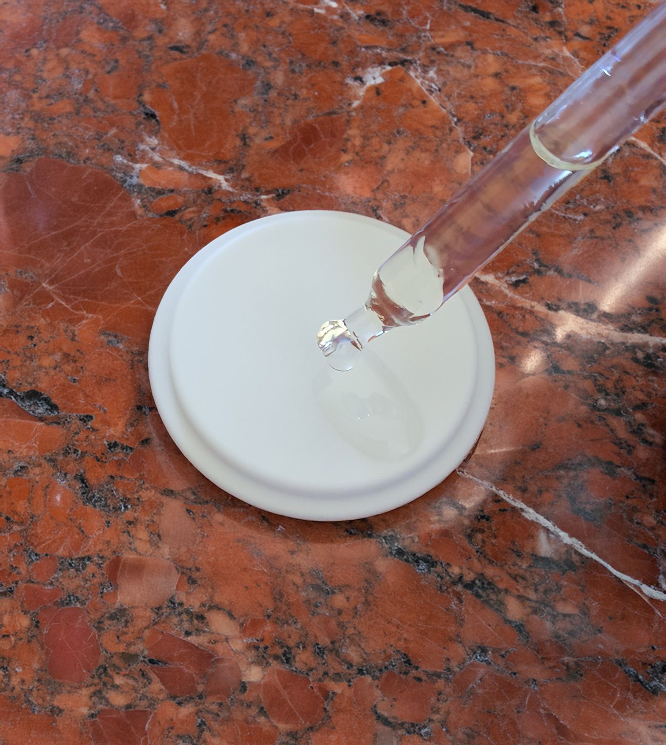Contagocce con liquido sopra una superficie bianca. Il liquido gocciola. Pipetta trasparente.