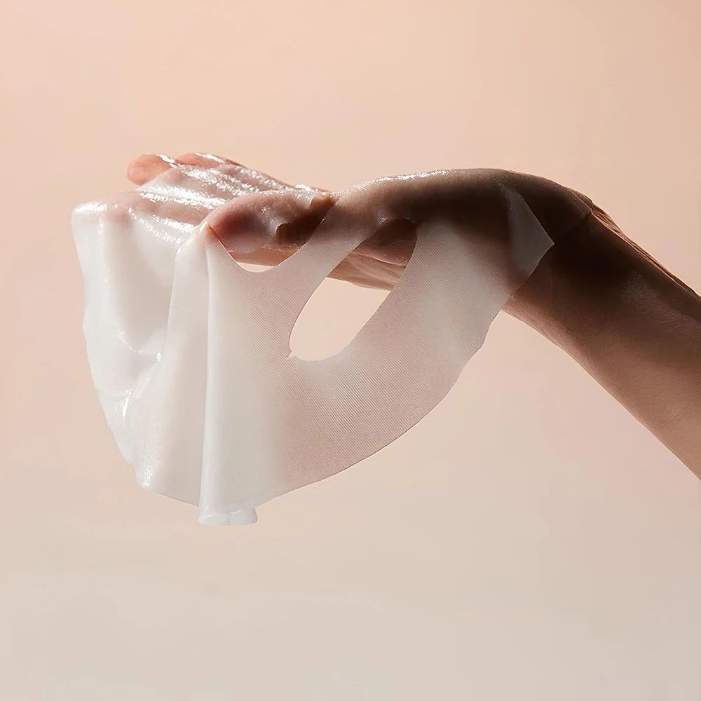 Una mano tiene una maschera per il viso bianca e umida. La maschera è trasparente e ha aperture per occhi e bocca.