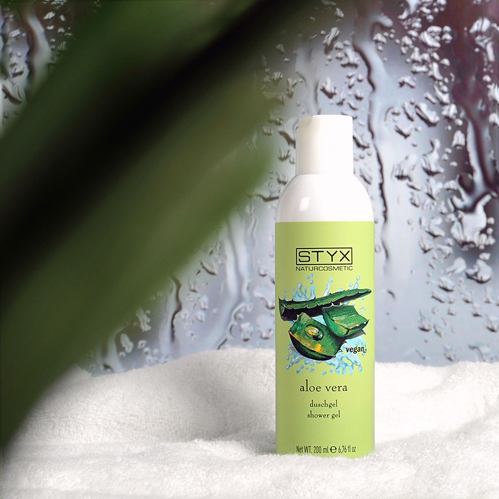 Flacone verde con tappo bianco su asciugamano bianco. Etichetta con illustrazione di aloe vera e testo: STYX Naturcosmetic, Aloe Vera Duschgel, vegan.