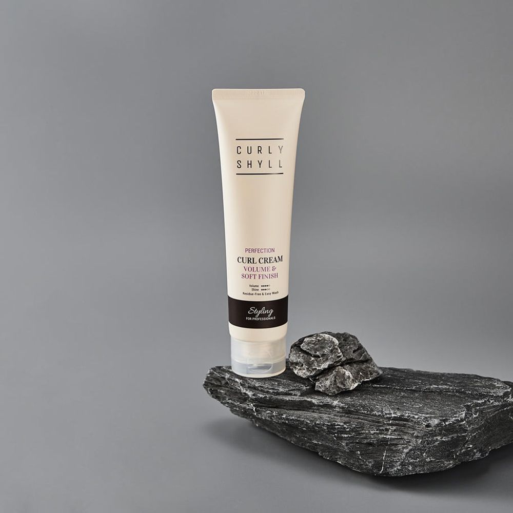 Tubo di crema posto su una pietra. Testo: CURLY SHYLL, Perfection Curl Cream, Volume & Soft Finish. Striscia nera con testo Styling.