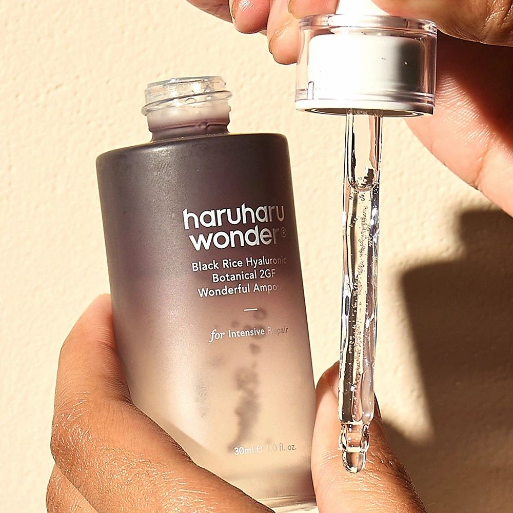 Mani che tengono flacone e pipetta di siero. Pipetta con siero. Scritta nera: haruharu wonder, Black Rice Hyaluronic Botanical 2GF Wonderful Ampoule.