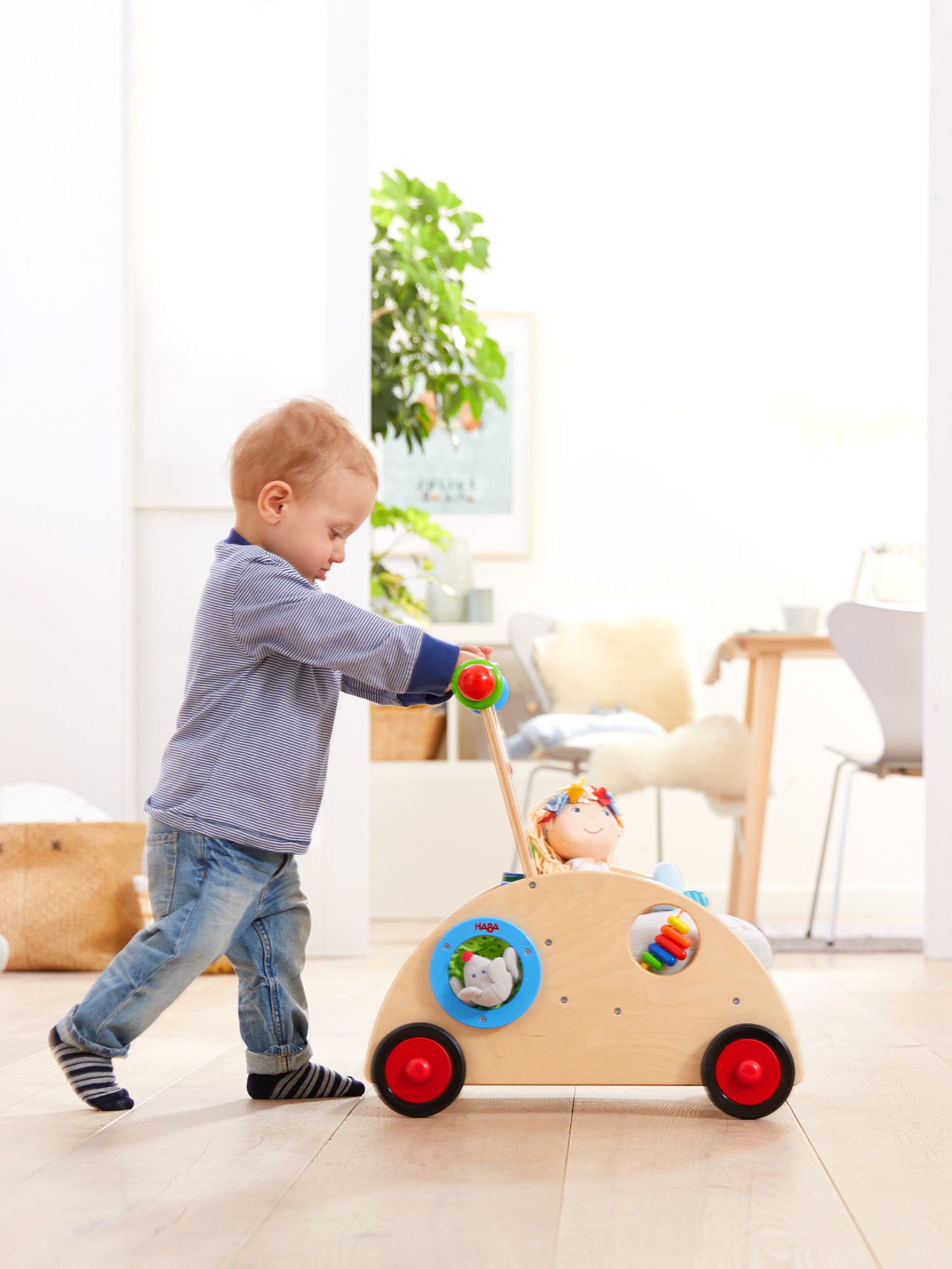 Bambino piccolo spinge un girello in legno. Il girello ha ruote, un manico e dei giocattoli.