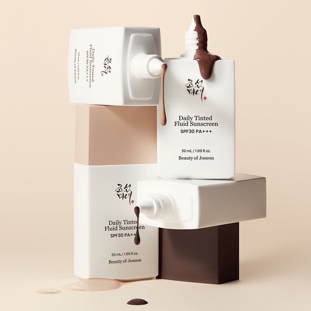 Tre flaconi BEAUTY OF JOSEON Daily Tinted Fluid Sunscreen, uno con liquido marrone.