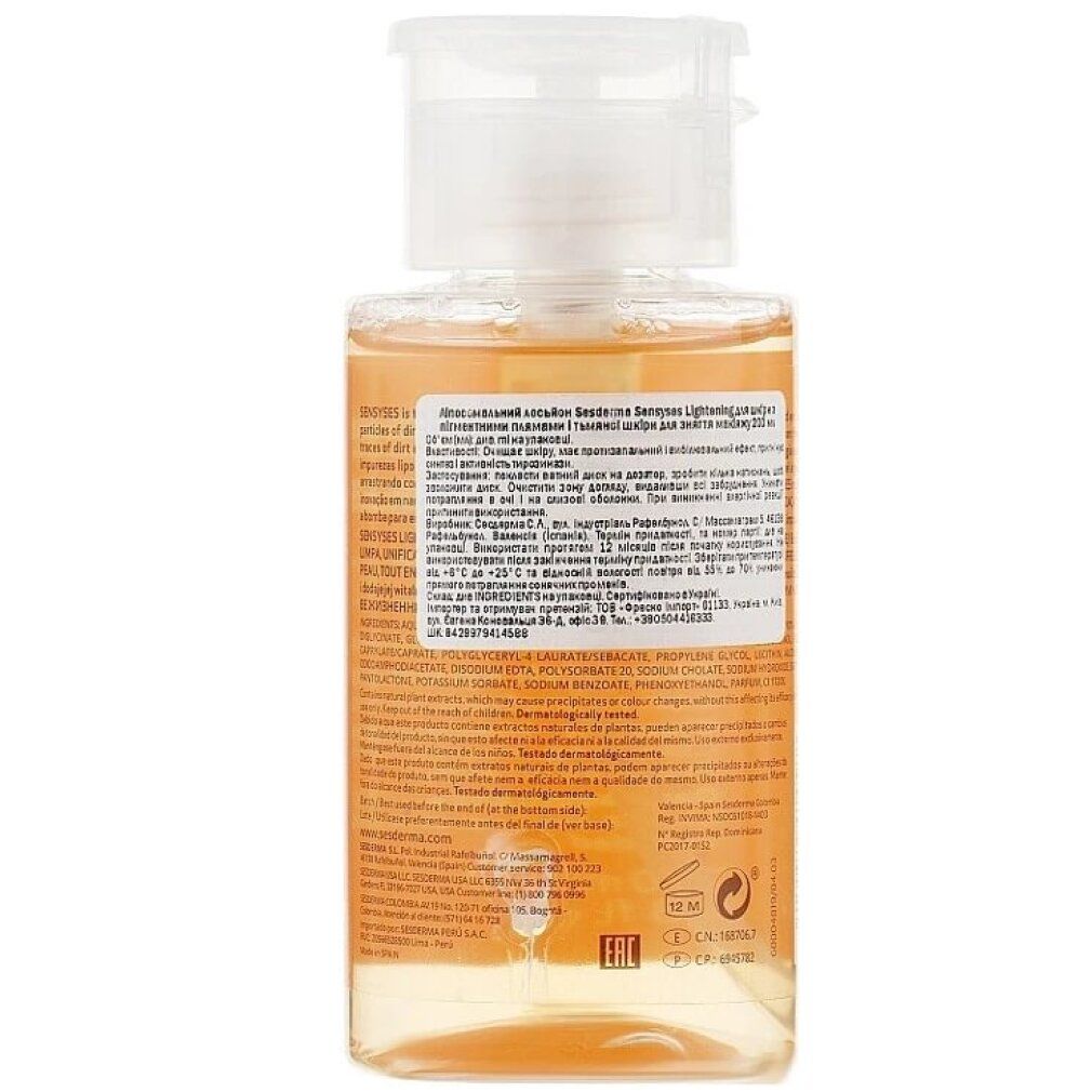 Mano che tiene un batuffolo di cotone sulla bottiglia. Bottiglia: Sesderma Sensyses Cleanser Lightening. Altri prodotti sullo sfondo.