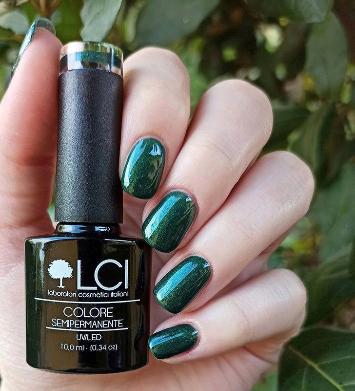 Mano con unghie smaltate e flacone di smalto. Smalto verde scuro. Scritta: LCI, Colore Semipermanente, UVLED.