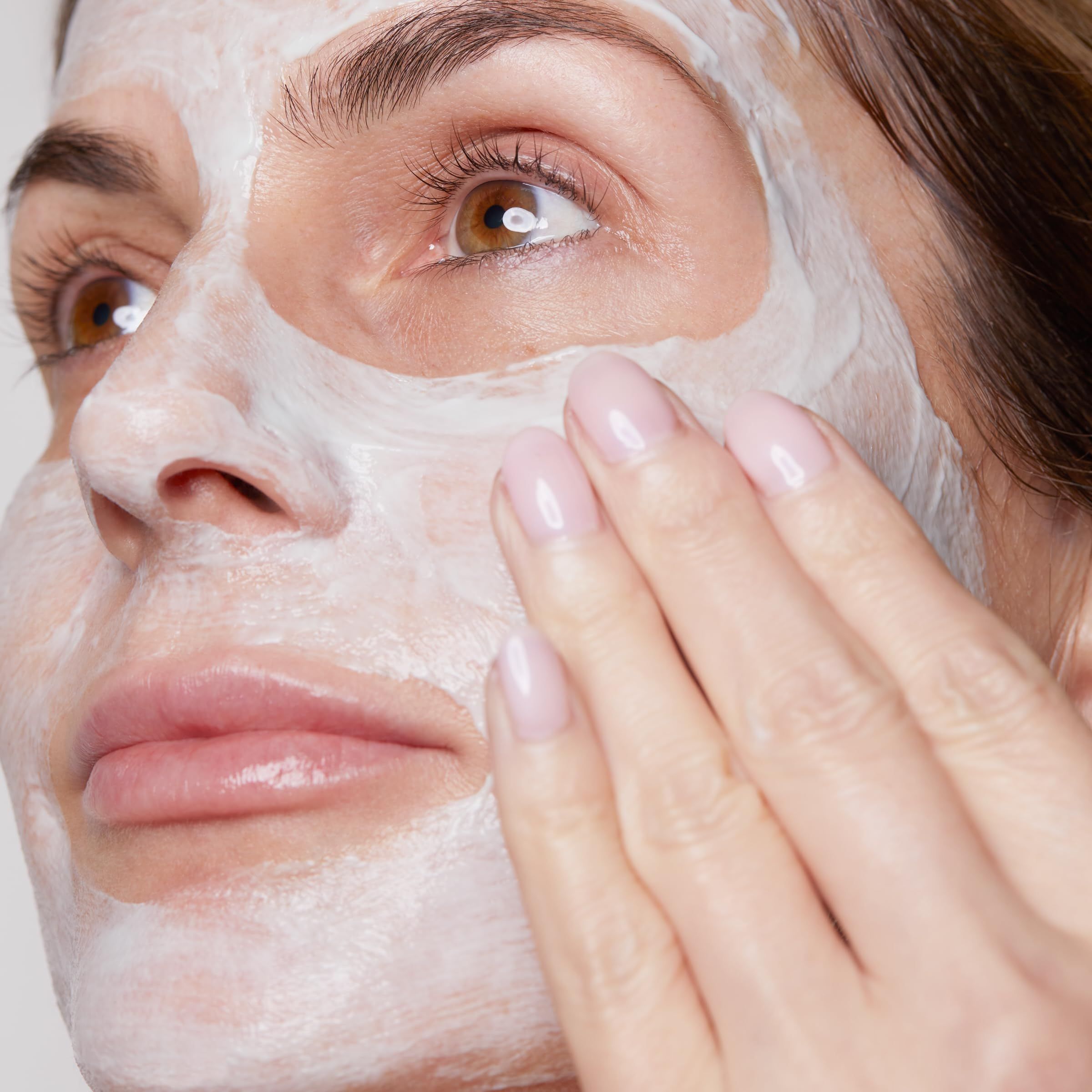 Primo piano di una donna che applica la crema sul viso. Pelle chiara, labbra rosa, manicure.