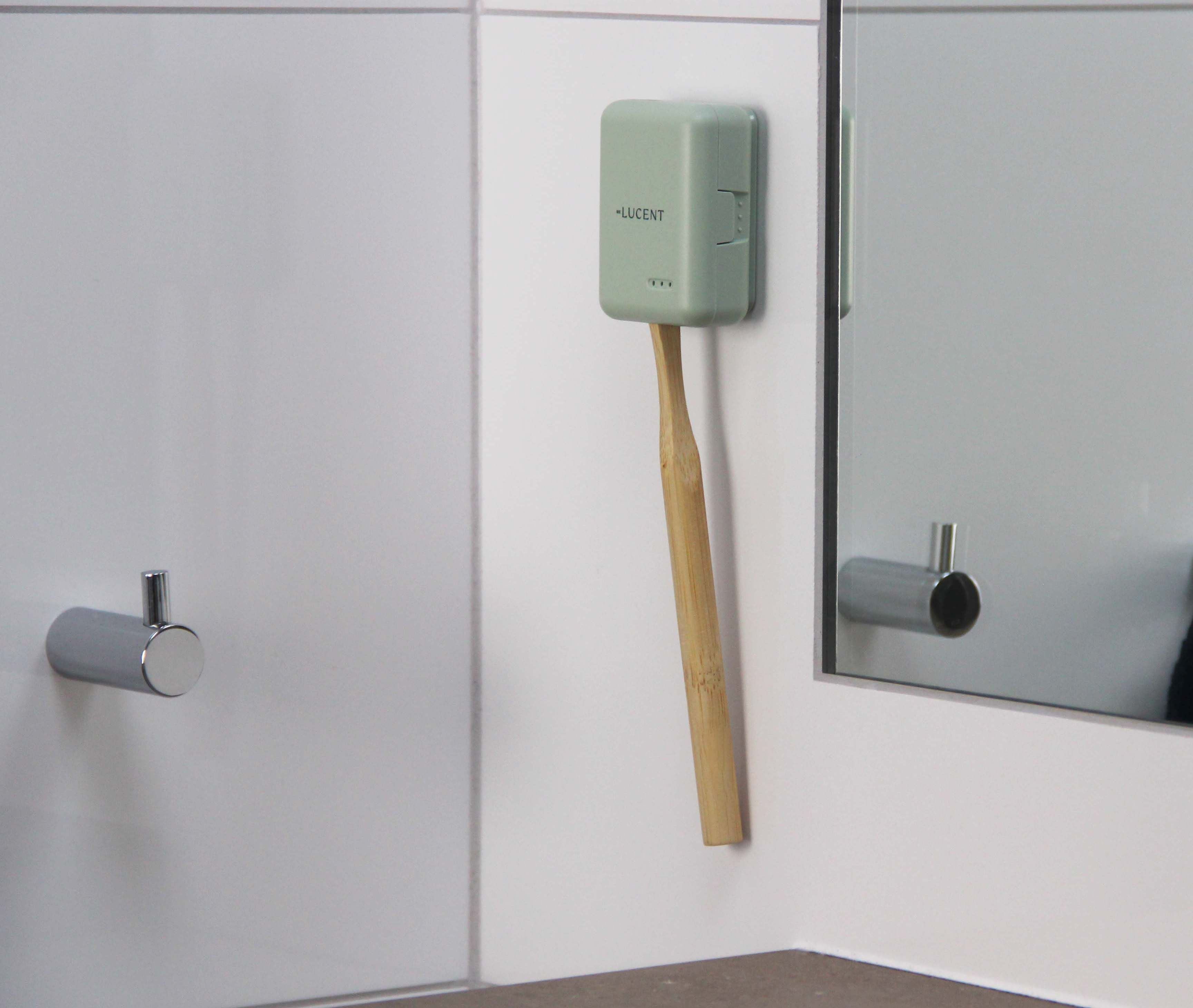 Custodia verde chiaro sul muro. Spazzolino inserito nella custodia. Specchio sullo sfondo.