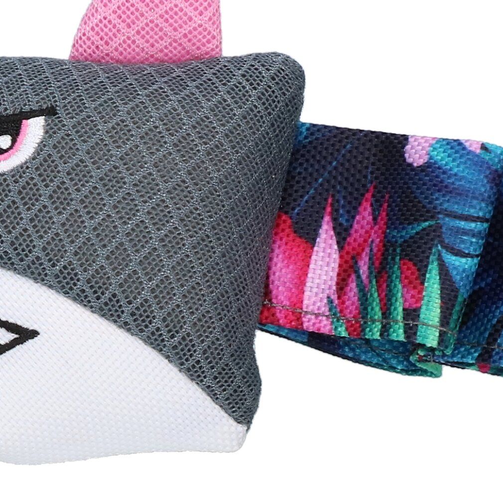 Primo piano di un giocattolo grigio con un design a squalo. La coda presenta un motivo tropicale. Il giocattolo ha una pinna rosa.