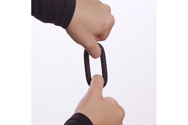 Anello nero allungato teso tra le mani. Sfondo bianco.