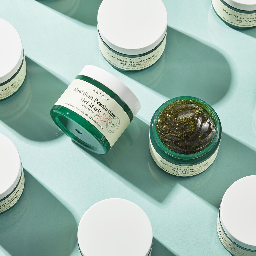 Diversi barattoli verdi di maschera su sfondo blu. Scritta: New Skin Resolution Gel Mask.