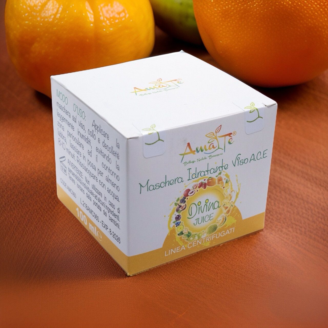 Confezione prodotto su fondo legno con arance. Scritta: Maschera Idratante Viso A.C.E. Divina Juice. Logo Amatè.