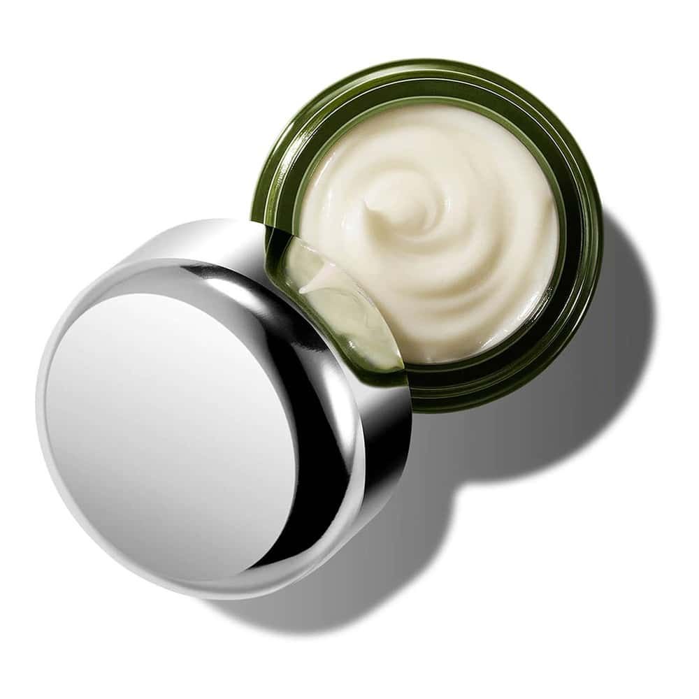 Vasetto verde aperto con sostanza cremosa e coperchio argentato. Il coperchio è appoggiato accanto su sfondo bianco.